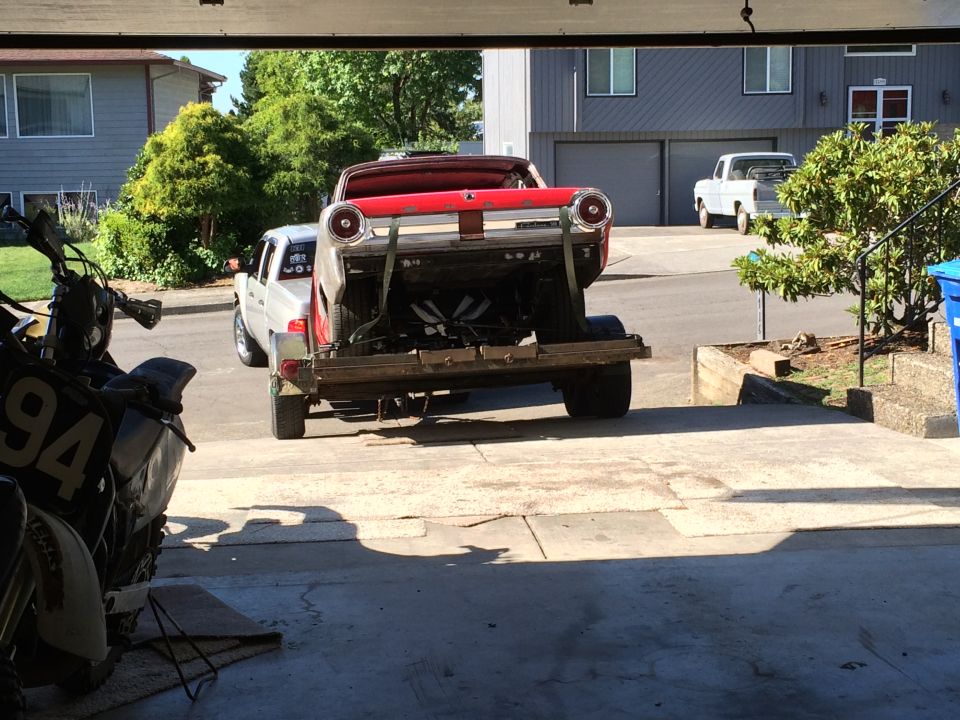 Red classic car on trailer towed by silver pickup truck, motorcycle in foreground.