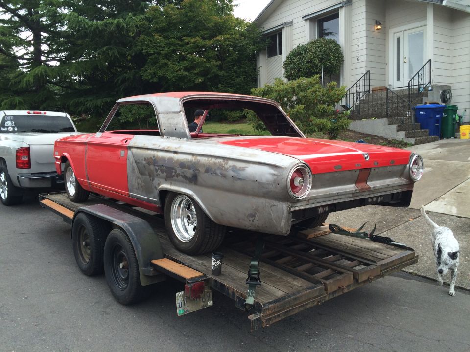1964 Ford Fairlane on a trailer being towed by a pickup truck.