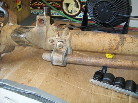 1991 Ford Bronco - A close-up view of a rusty, heavy-duty vehicle axle assembly with attached steering components. A set of socket wrenches is visible in the…