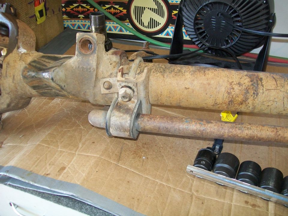 Rusty vehicle axle assembly with steering linkage and socket wrenches.