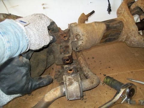 1991 Ford Bronco - A person wearing work gloves is holding a rusty metal automotive suspension component. Tools are visible on the floor nearby.