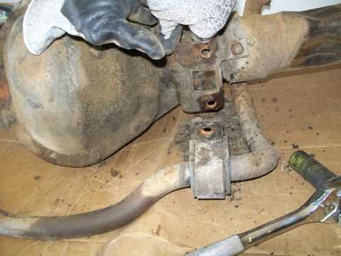 1991 Ford Bronco - A close-up view of a rusty rear axle assembly with a sway bar attached. A gloved hand is visible, appearing to work on bolts securing the a…