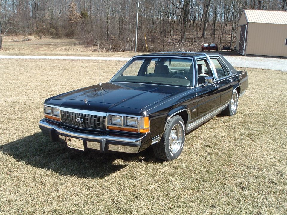 Black Ford LTD Crown Victoria sedan, front three-quarter on a dry lawn