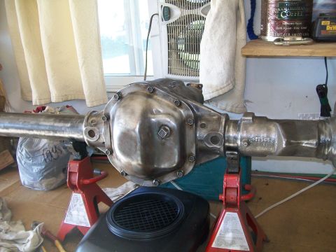 1991 Ford Bronco - A polished metal rear axle assembly, likely from a 1991 Ford Bronco, is supported by red jack stands in a garage setting. The differential…