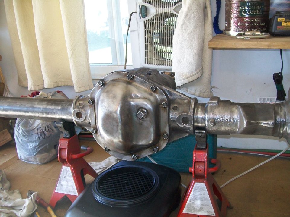Polished metal rear axle assembly on red jack stands in a garage.