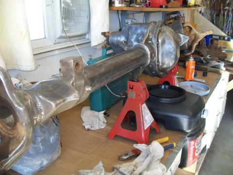 1991 Ford Bronco - A differential housing assembly is supported by red jack stands on a workbench. Tools and a drain pan are visible nearby.