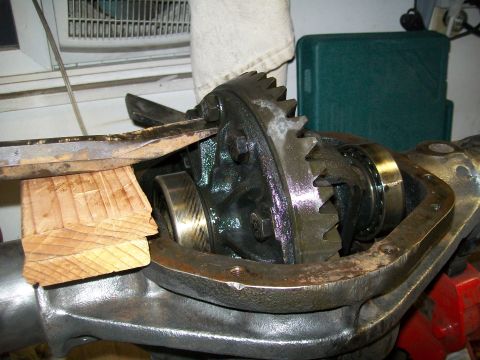 1991 Ford Bronco - A close-up view shows a differential assembly with a large gear and bearing. A metal pry bar is being used with a wooden block to adjust th…