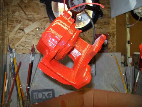 1991 Ford Bronco - A bright orange painted part, possibly a brake caliper or similar component, is suspended by a red rope against a background of plywood wal…