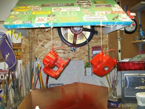 1991 Ford Bronco - Two bright orange painted brake calipers hang from strings under a green canopy covered in stickers. A variety of paintbrushes and other to…
