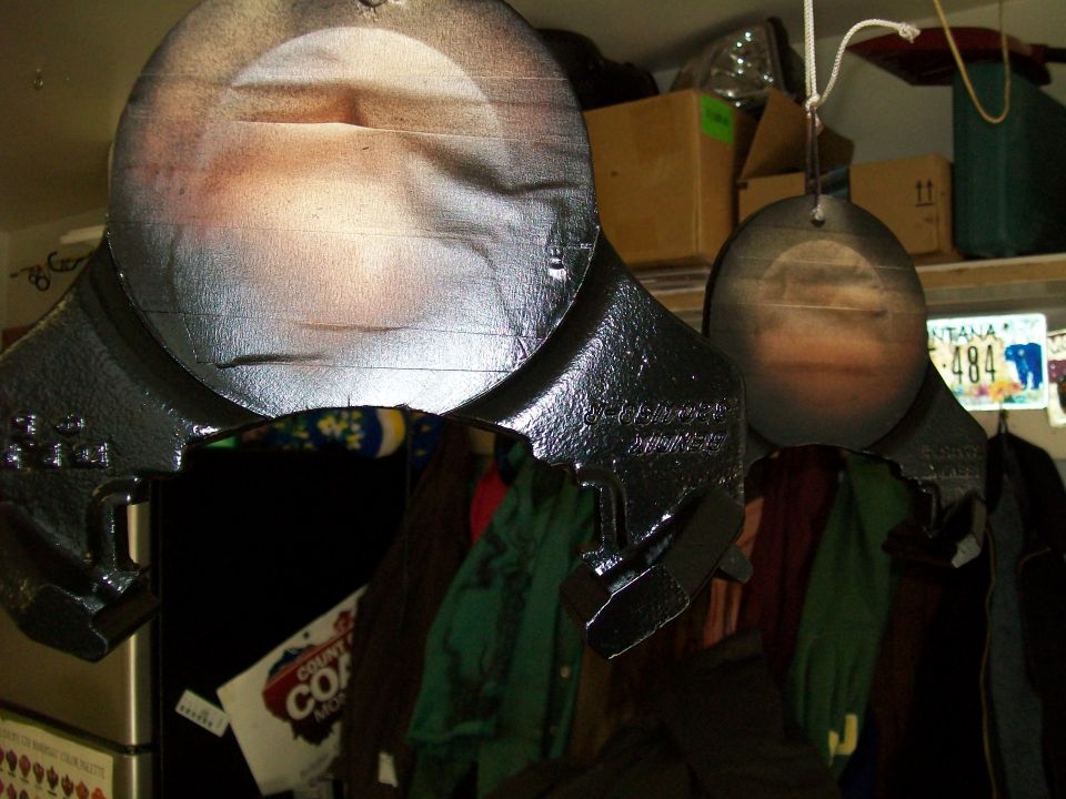 Two black metal targets hanging, one slightly larger than the other, with a Montana license plate in the background.