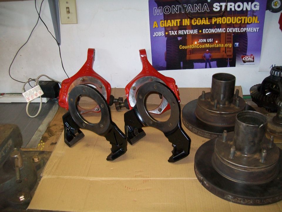 Two red and black brake caliper assemblies with brake rotors and hubs in the background.