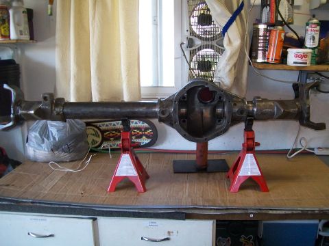 1991 Ford Bronco - A rear axle assembly is mounted on two red jack stands on a workbench. The axle is a heavy-duty metal component with a differential housing…