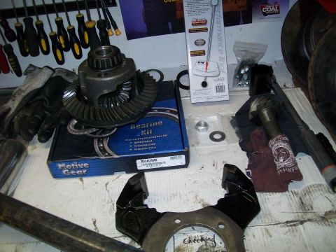 1991 Ford Bronco - A differential and bearing kit are laid out on a workbench with various tools and parts, including a torque wrench and brake rotor.