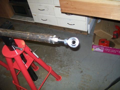 1991 Ford Bronco - A close-up view of a metal rod with a spherical joint attached, resting on a red jack stand. The background shows a filing cabinet and some…