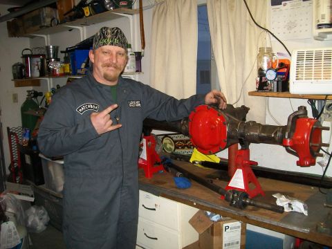 1991 Ford Bronco - A man in dark grey overalls poses with a vehicle rear axle assembly that has been painted red on the differential cover and end housings. T…