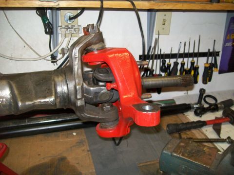 1991 Ford Bronco - A close-up view of a vehicle's front axle assembly, featuring a red-painted steering knuckle and a greased universal joint connected to a s…