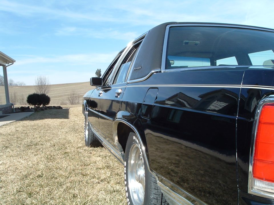 Rear-quarter detail of black Ford sedan roofline and taillight against fields