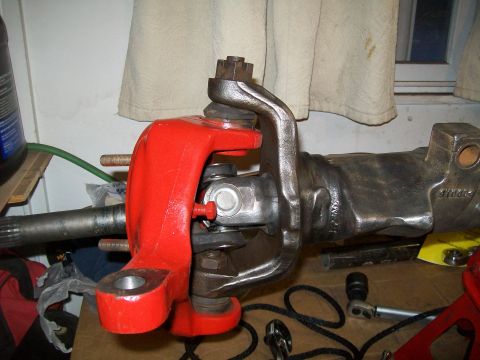 1991 Ford Bronco - A close-up view of a red painted steering knuckle assembly attached to a dark metal axle housing, likely part of a 1991 Ford Bronco build.
