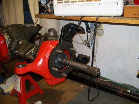 1991 Ford Bronco - A red painted axle assembly with a black brake caliper bracket is mounted on a red jack stand. The assembly appears to be part of a vehicle…