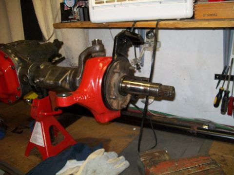1991 Ford Bronco - A red painted axle housing assembly, likely from a 1991 Ford Bronco, is supported by a red jack stand on a wooden workbench. The assembly i…