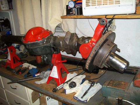 1991 Ford Bronco - A rear axle assembly, likely from a 1991 Ford Bronco, is supported by red jack stands on a workbench. The differential cover is painted red…