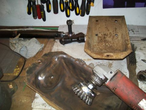 1991 Ford Bronco - An angle grinder with a wire brush attachment is being used to clean a rusty metal part on a workbench. Tools and other metal parts are vis…