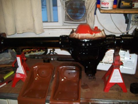 1991 Ford Bronco - A black rear axle assembly is supported by red jack stands on a workbench. A differential housing with a red protective cover is visible in…