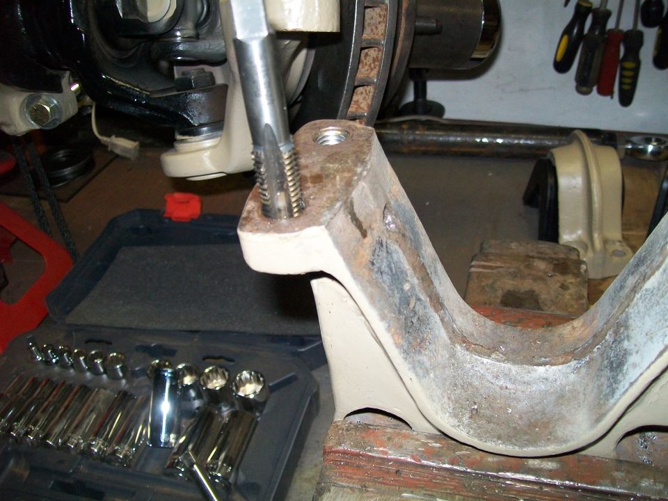 Tapping a suspension part with a tool, toolbox with sockets in foreground.