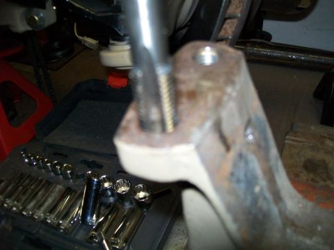 1991 Ford Bronco - A close-up shot shows a rusty metal bracket with a bolt threaded into it, resting on a toolbox filled with various sockets. The bracket app…