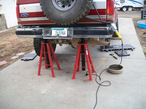 1991 Ford Bronco - The rear of a red Ford Bronco is supported by red jack stands. A license plate reading "29-9246A" is visible on the chrome bumper.