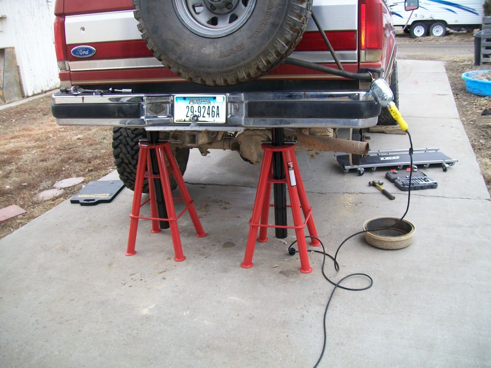 Red 1991 Ford Bronco rear end on jack stands, chrome bumper, license plate.