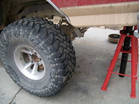 1991 Ford Bronco - A close-up view of a large, off-road tire on a red vehicle, supported by a red jack stand. The tire is a Toyo Open Country M/T.
