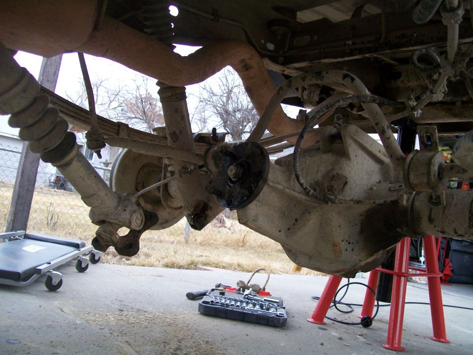 Underside of a vehicle's rear suspension with tools on the ground.