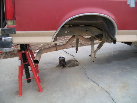 1991 Ford Bronco - The rear underside of a red and tan Ford truck is supported by red jack stands. The exhaust system is disconnected, and the rear shocks are…