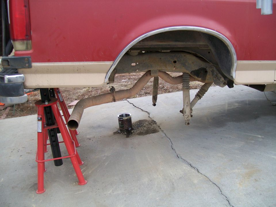 Rear underside of a red and tan truck on jack stands, exhaust removed, shocks off