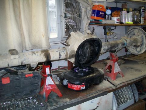 1991 Ford Bronco - A disassembled rear axle assembly, likely from a 1991 Ford Bronco, is supported by red jack stands on a workbench. A drain pan sits beneath…