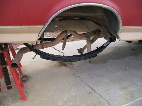 1991 Ford Bronco - The underside of a red and tan 1991 Ford Bronco shows the rear suspension with new leaf springs installed. The vehicle is supported by red…