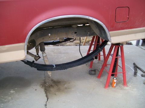 1991 Ford Bronco - The rear suspension of a red and tan Ford Bronco is supported by red jack stands, revealing leaf springs and a shock absorber. The vehicle…