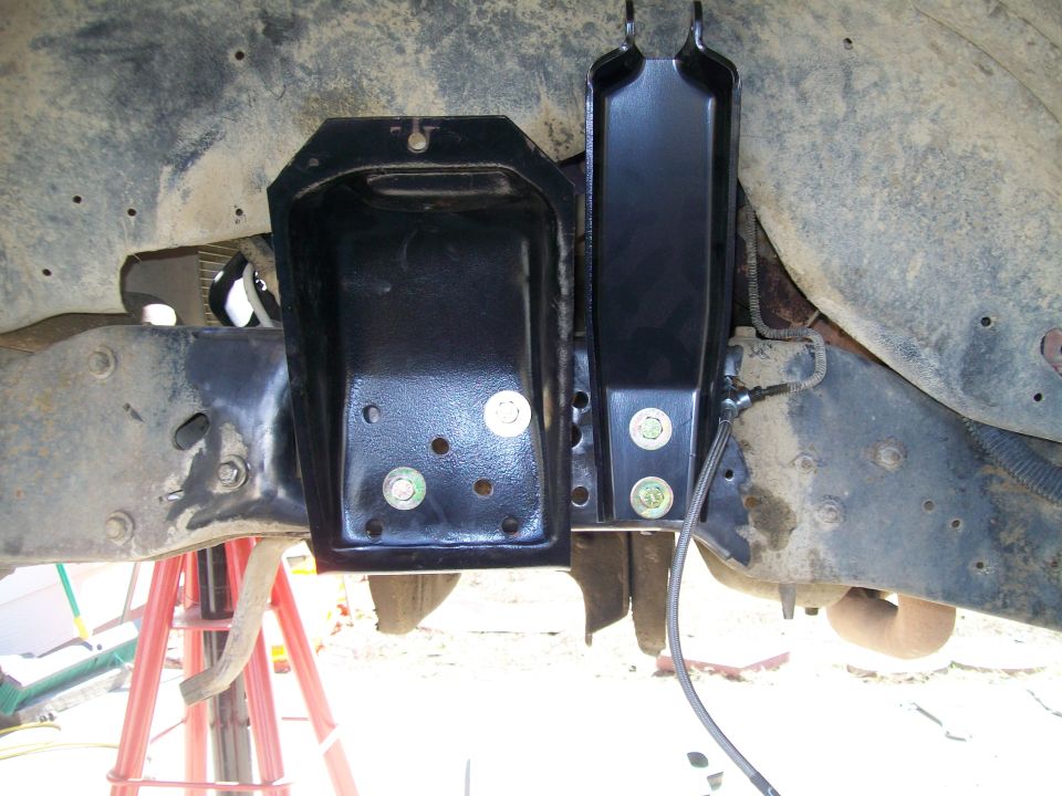 close-up of black metal brackets bolted to a vehicle's frame, with some suspension parts visible