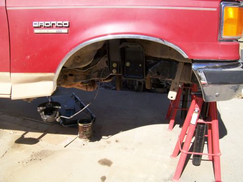 1991 Ford Bronco - A red and tan Ford Bronco is shown with its front wheel removed and the vehicle supported by jack stands.