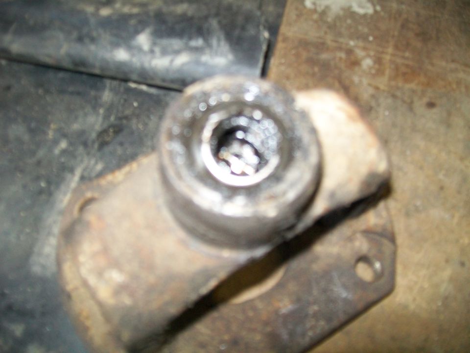 Close-up of a rusty, worn metal part with a circular opening, possibly a u-joint or bearing housing