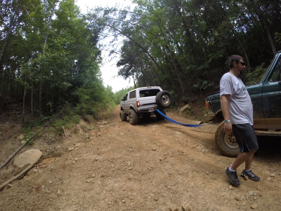 Silver SUV with spare tire on back being towed by green SUV on dirt road