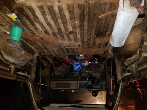 1979 Ford Bronco - The interior of a 1979 Ford Bronco features a dashboard, steering wheel, and a rusted floor with a spool of wire and a muffler visible.