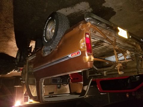 1979 Ford Bronco - A brown SUV is overturned on its side, revealing its interior and rear-mounted spare tire.