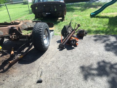 1979 Ford Bronco - Disassembled vehicle parts are spread out on a driveway in a grassy yard with a slide in the background.