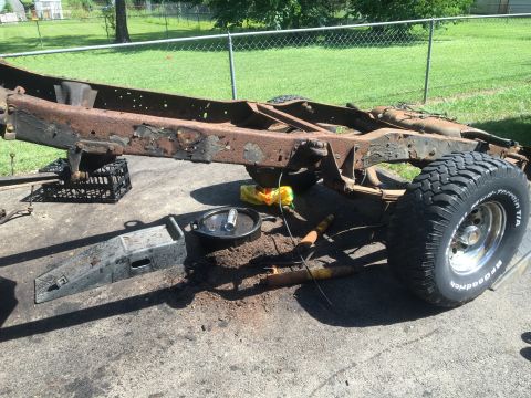 1979 Ford Bronco - A heavily rusted vehicle frame sits on pavement with a single tire attached.