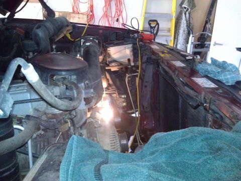 1996 Ford Bronco - Close-up view of a vehicle's engine bay, partially covered by a teal towel and surrounded by tools and electrical cords.