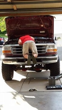 1996 Ford Bronco - Mechanic works on the engine of a red Ford F-Series truck in a garage.