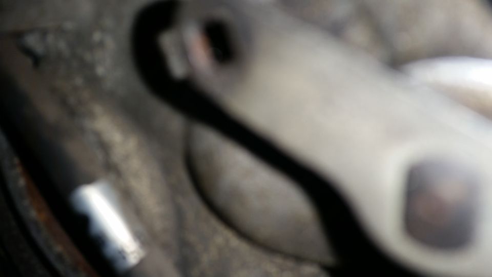 Blurry close-up of a light gray metal automotive part with dark shadows and rust.