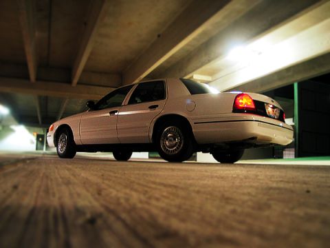 2000 Ford Crown Victoria - A white 2000 Ford Crown Victoria is parked in a dimly lit indoor area, its rear lights glowing.